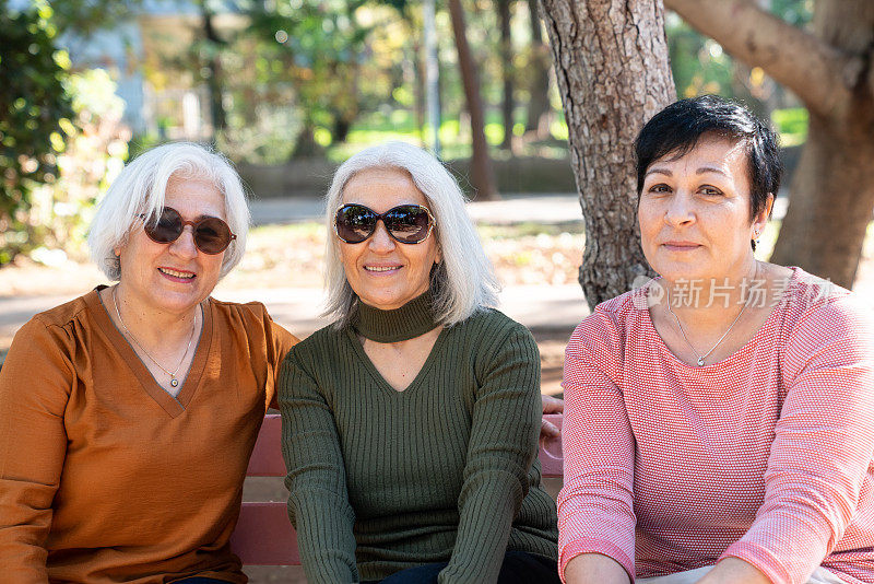 三位高级女性朋友坐在公共公园的长椅上
