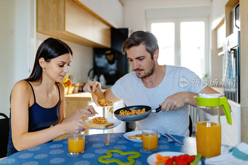 一个年轻的女人在桌子旁为她的丈夫端着盘子倒煎蛋卷