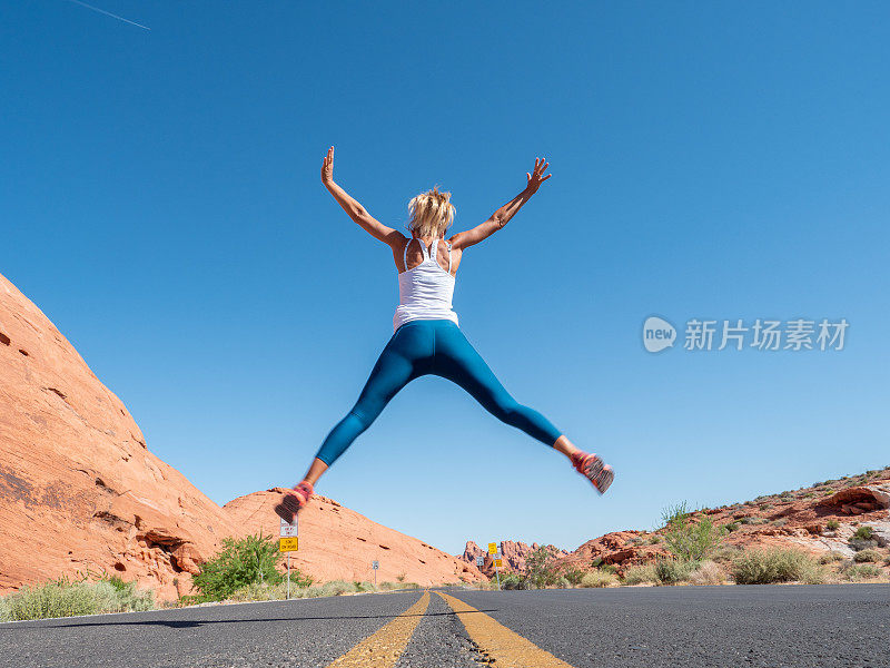 快乐的女孩在公路中间跳得很高，女人在内华达州的空旷高速公路上跳