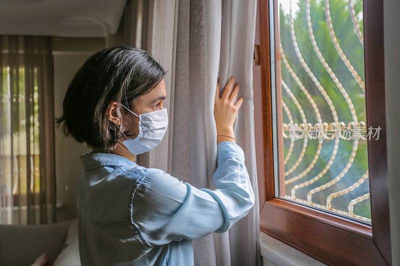 年轻女子戴着医用口罩望着窗外