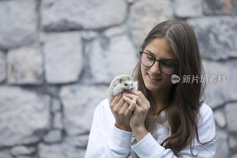 微笑的年轻成年妇女抱着和看她的宠物刺猬在户外