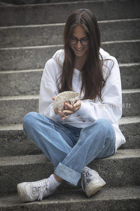 微笑的年轻女子坐在楼梯上，抱着她的宠物刺猬