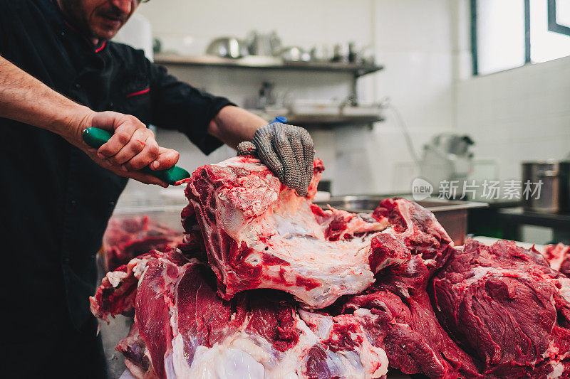 男屠夫在餐厅厨房用刀切生牛肉