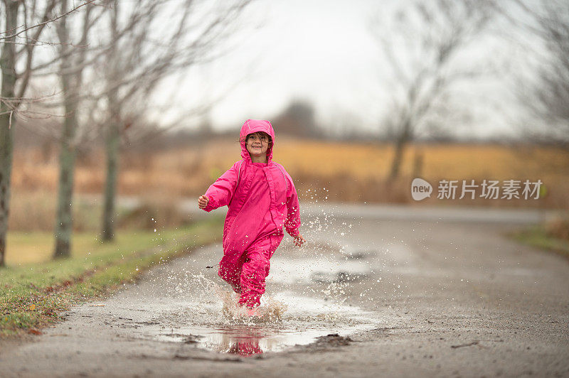 女孩跑过雨水坑在粉红色的雨衣