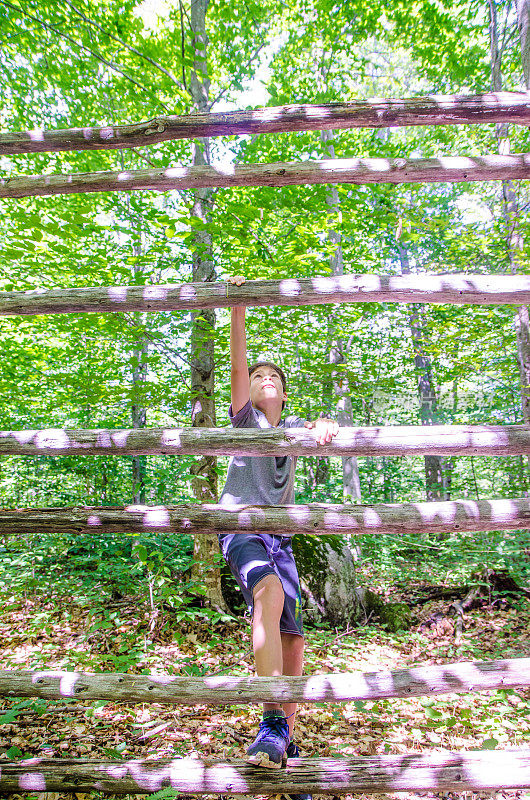 男孩爬在森林的木结构上