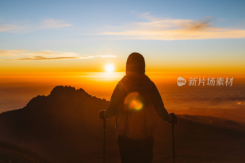 一名女性徒步旅行者在乞力马扎罗山山顶享受敬畏的日出，实现了自己的梦想