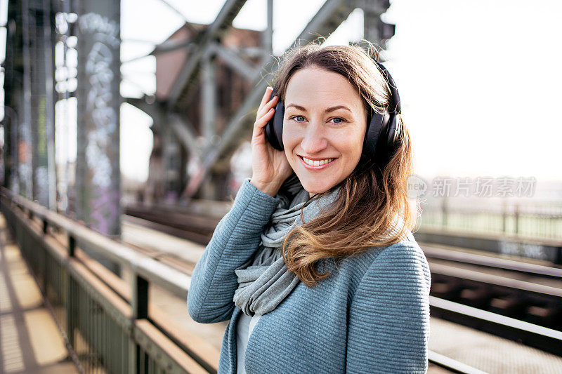 女子站在铁路桥上，戴着耳机，面带微笑