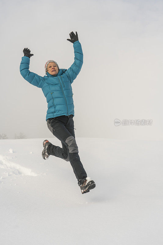 成熟的女人穿着皮大衣在雪地上跳起来