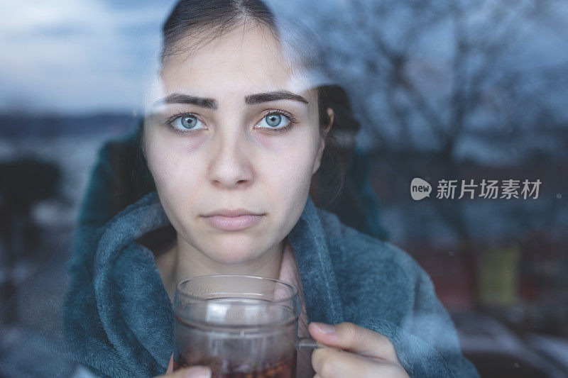 感染流感的女人透过窗户看起来很悲伤