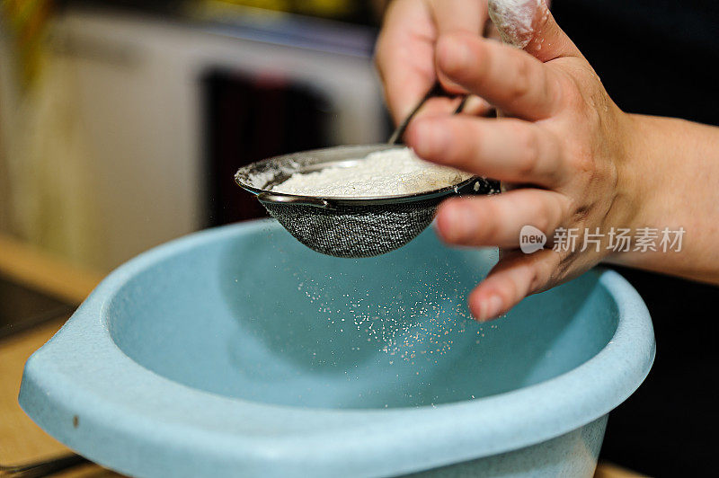 厨房里的一位妇女正在用金属过滤器筛面粉。