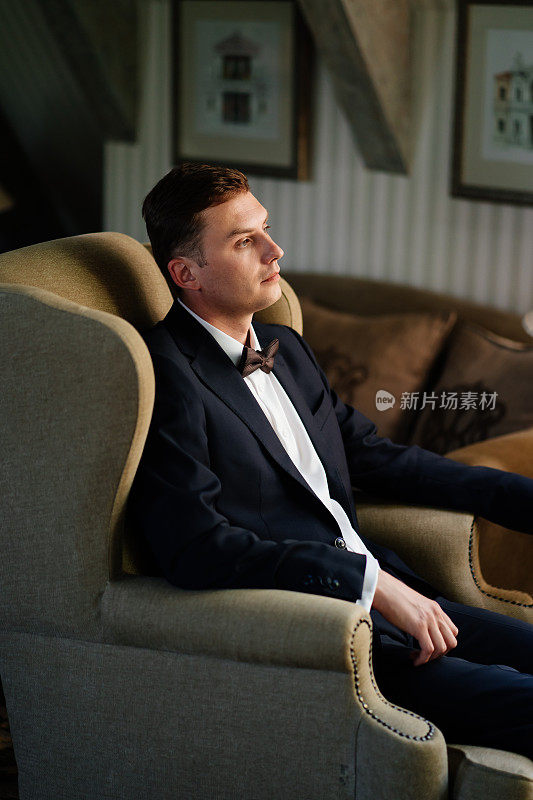 一张男人的肖像，穿着西装，打着领结坐在椅子上。新郎。