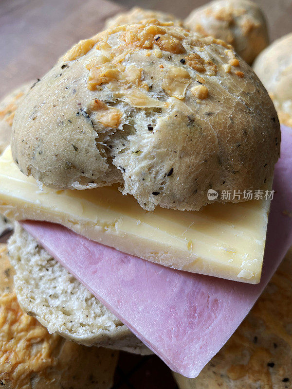 近景:新鲜烘焙的自制谷物面包，木制砧板上的香草奶酪面包，切开的面包卷，夹满火腿片和切达奶酪，准备做三明治，高架视野