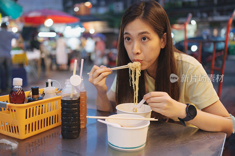 年轻的z一代本地亚洲人周末快乐使用智能手机5G互联网社交媒体前吃鱼丸面在中国城的街头小吃泰国曼谷耀瓦