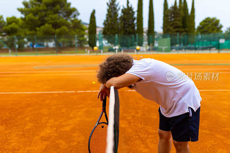 网球运动员，在比赛间隙靠在网球网上放松