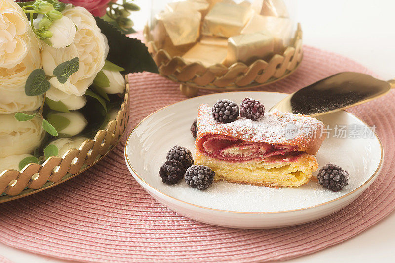 白色桌子上的粉色餐巾纸上有新鲜浆果、鲜花和一杯茶。传统的开胃菜或早餐。斯堪的纳维亚式菜肴和梗类犬。