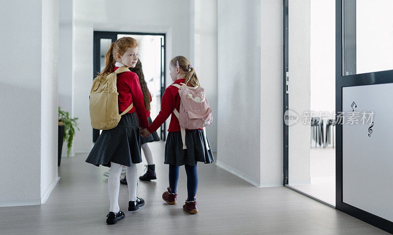 快乐的女学生与唐氏综合症同学穿着制服走在学校走廊与同学，后视图。
