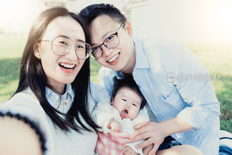 快乐的亚洲家庭对着相机自拍——笑着的中国年轻人和她的小孩在公园里玩得很开心——快乐的夫妇和她的小儿子。爱的概念。跨种族的人