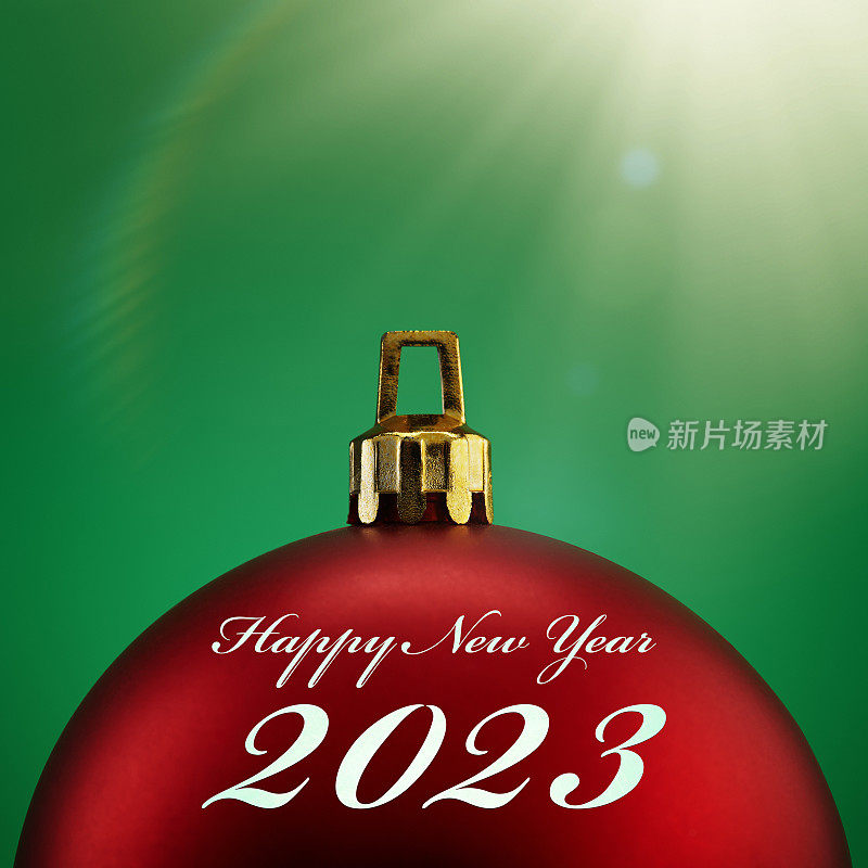 红色圣诞球在绿色背景与阳光和镜头耀斑与2023新年快乐的文字。假期，圣诞节和新年的概念