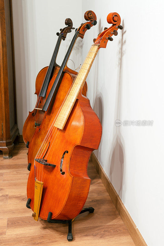 垂直拍摄的大提琴和小提琴在木地板上，旁边的室内白墙