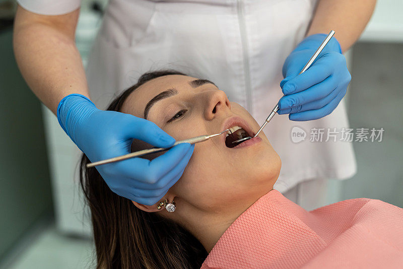 女牙医用牙科镜和不锈钢工具检查病人的牙齿