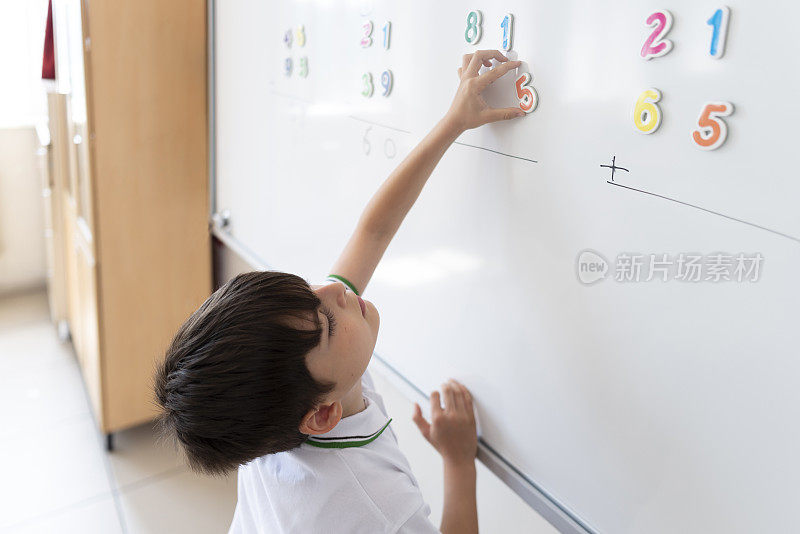 小学生穿着校服用白板上的磁性数字解数学题。