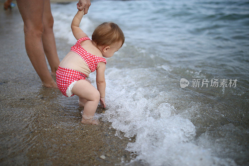 宝宝在海边散步，和妈妈一起学走路。第一步，父母的关怀和爱的概念库存照片