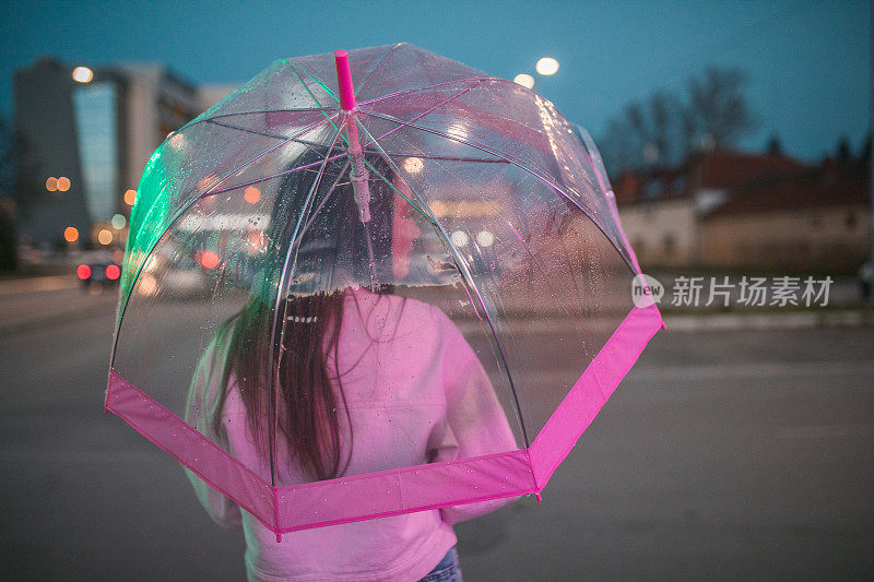 一位千禧一代女性在雨夜撑伞行走的后景