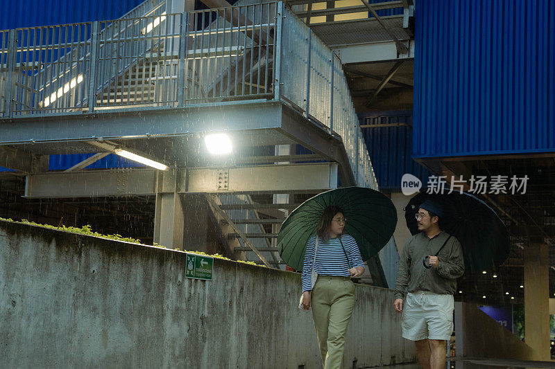 一对亚洲夫妇在下雨天打着伞一起散步