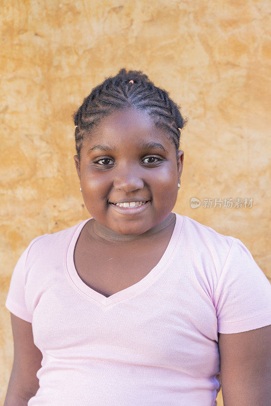 快乐的年轻美国黑人女孩的肖像在户外墙的背景前微笑