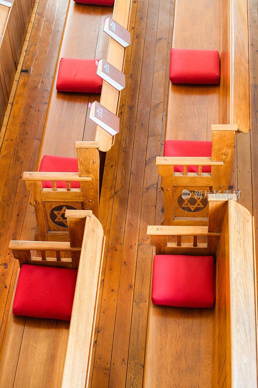 木制的犹太教堂长凳上有红色的枕头，大卫之星正上方