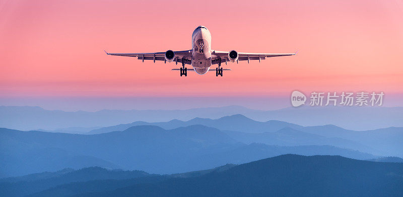 夕阳下，飞机在粉红色的天空中飞行。风景与客机飞越山脉在雾，红色的天空在黄昏。飞机正在降落。业务。鸟瞰图。交通工具。私人飞机