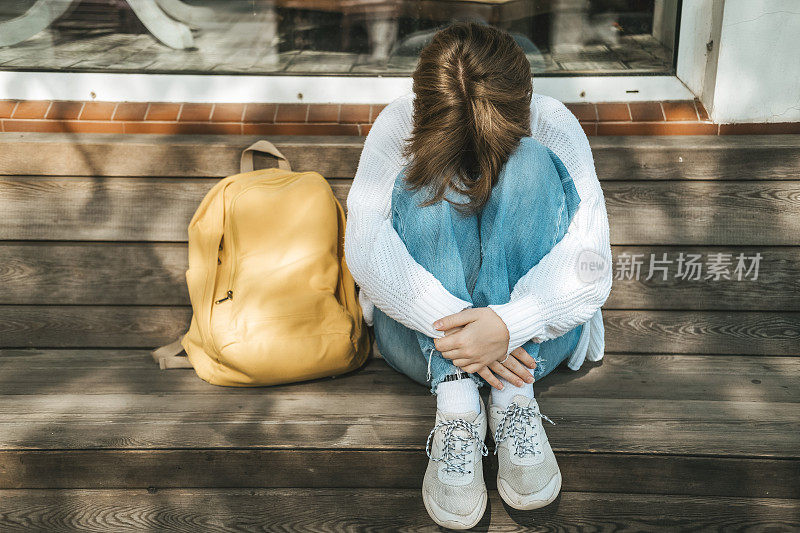 十几岁的女学生坐在长凳上，把脸埋在膝盖里，秋天的沮丧，学校的困难