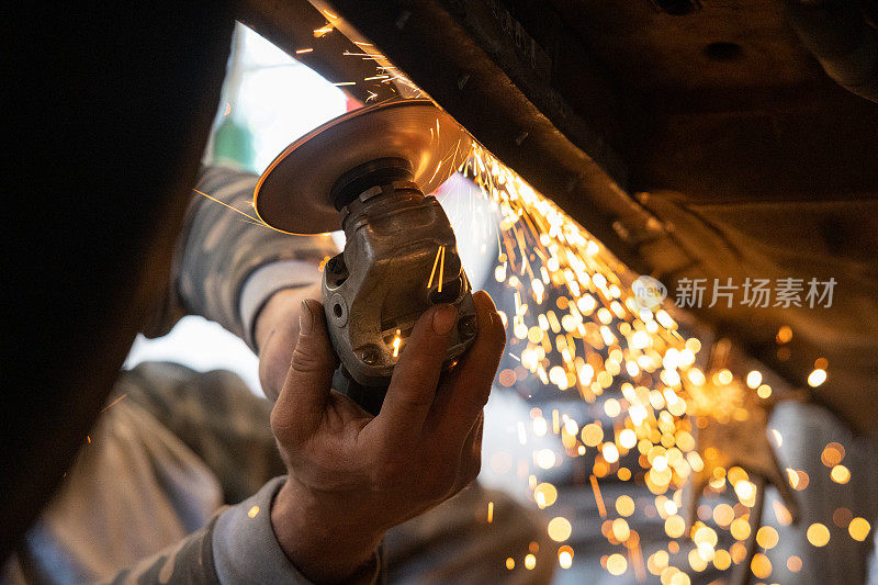 机械师用磨床除去汽车上的锈。