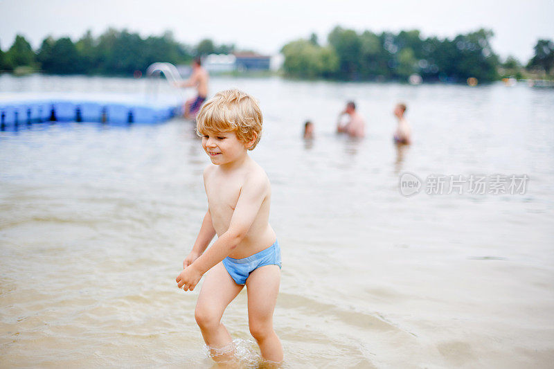 一个金发碧眼的学前班小男孩在夏日户外的湖里戏水。快乐的孩子学游泳。假期和孩子一起积极休闲。国内湖泊的危险