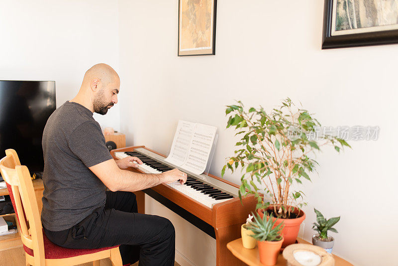 一个成年男子正在家里弹奏数码钢琴