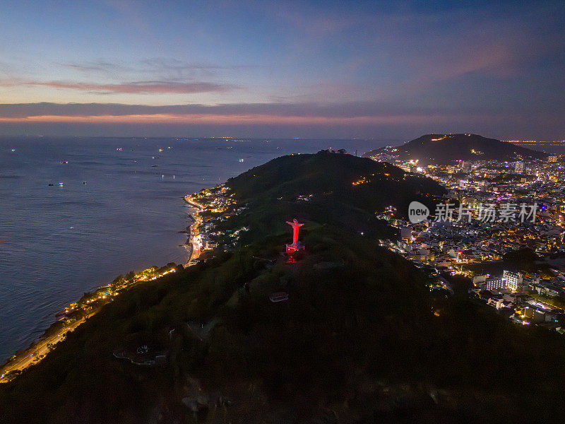 从上面俯瞰云头海岸全景，海浪、海岸线、街道、椰子树、越南Nho山后面的基督国王雕像