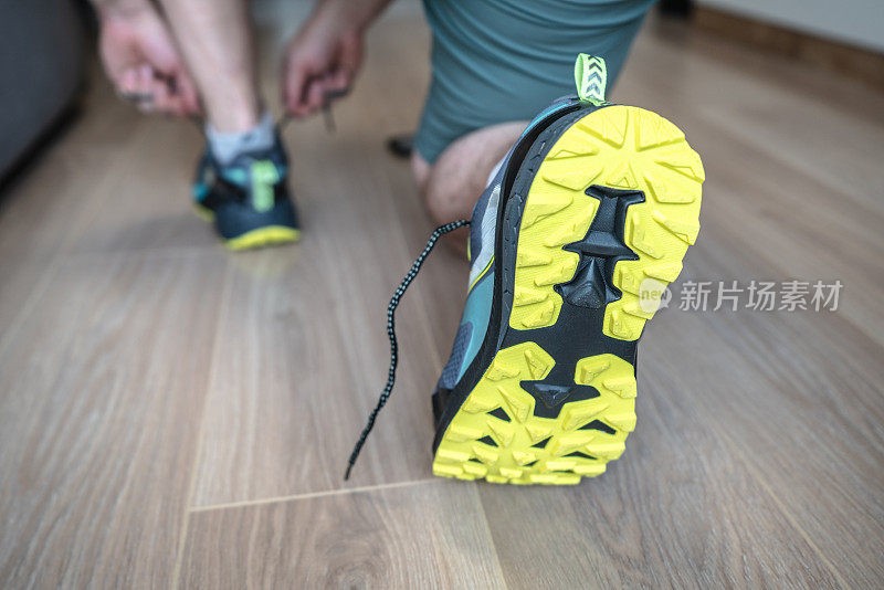 一个男人把鞋带系在运动鞋上，准备早上锻炼或越野跑。注意运动鞋的鞋底
