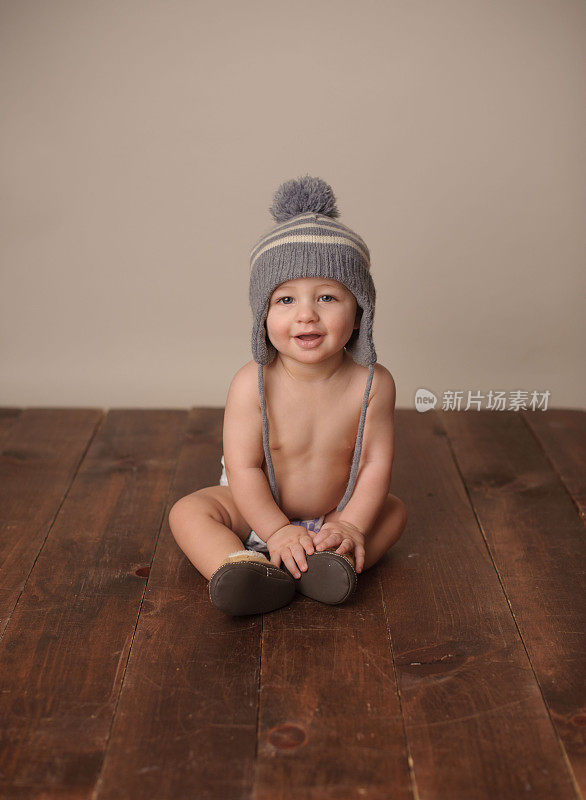 婴儿戴着针织帽坐在木地板上