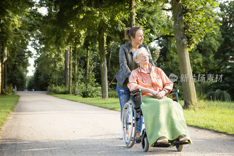 一个年轻女子推着一位坐轮椅的老妇人穿过公园