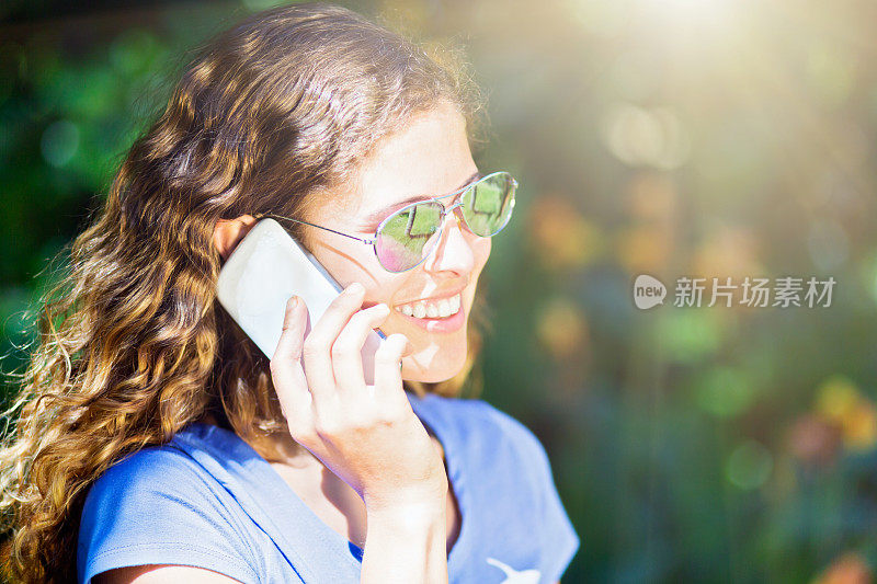 美丽的卷发女孩在阳光下用手机聊天