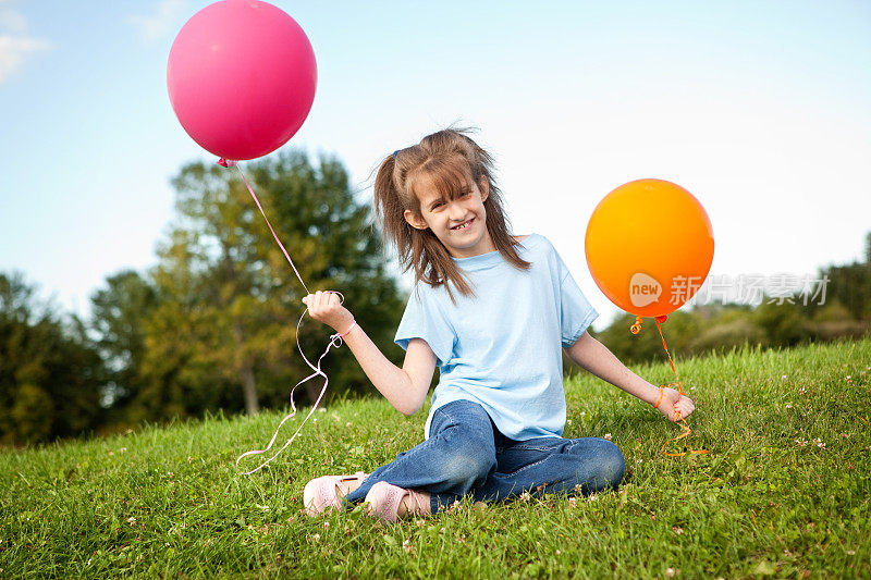 小女孩坐在草地上，拿着气球