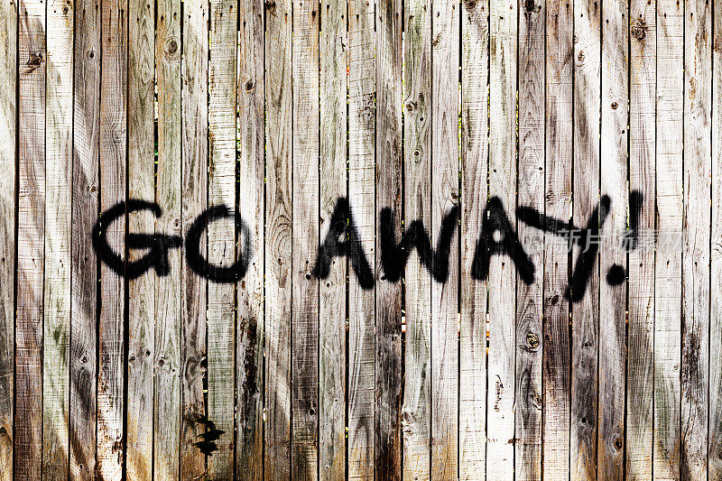 木栅栏上不友好的涂鸦写着“走开!”