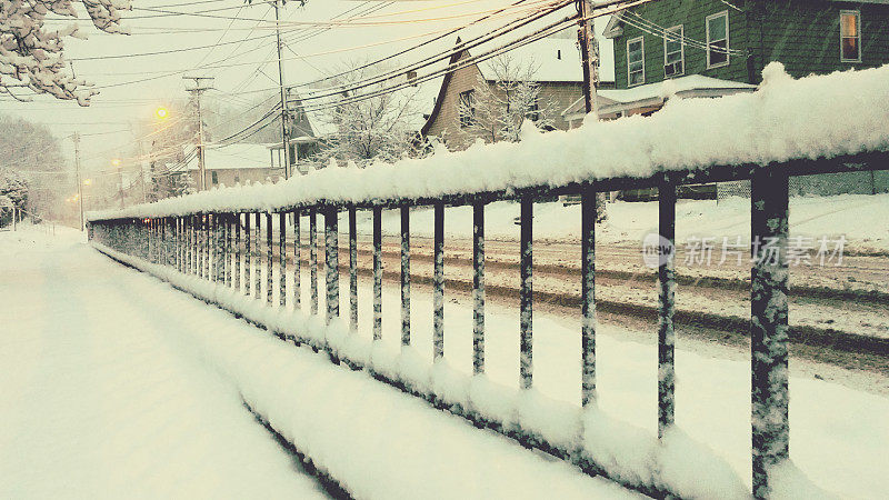黑雪覆盖的金属栅栏沿街道和房屋