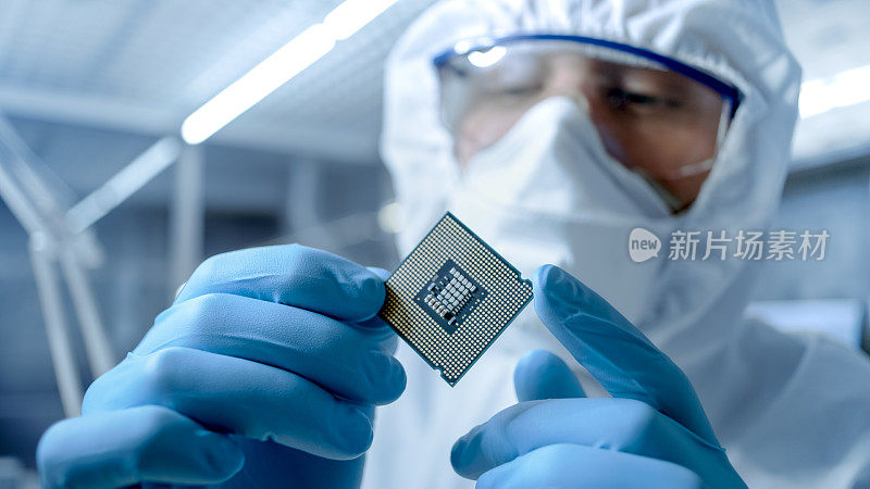 在超现代电子制造工厂，无菌工作服的设计工程师手持手套并检查微芯片。