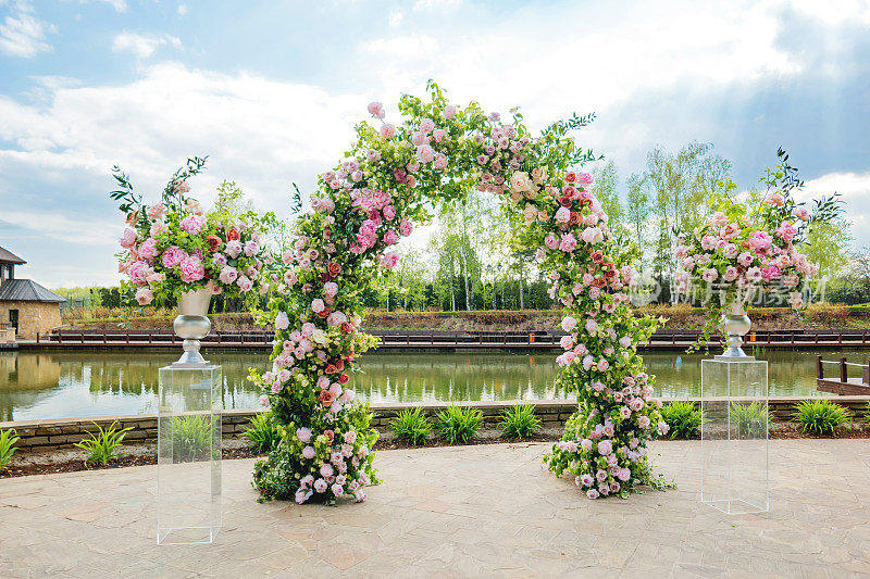 婚礼上美丽的花拱门。装着粉红玫瑰和牡丹的花瓶。婚礼安排在户外公园附近的池塘。