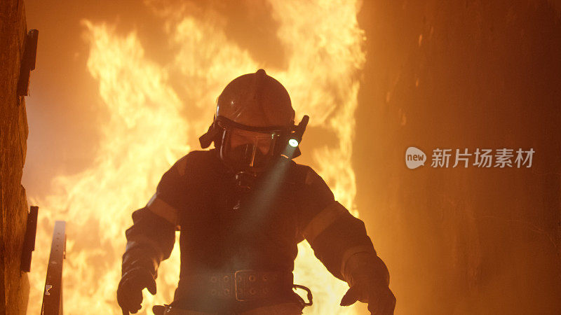 勇敢的消防员在头盔上打开手电筒跑下燃烧的楼梯。火是激烈的。