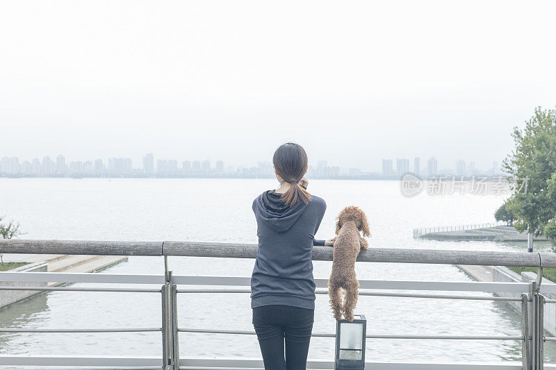 后视图的女人和可爱的小狗靠在栏杆上看风景