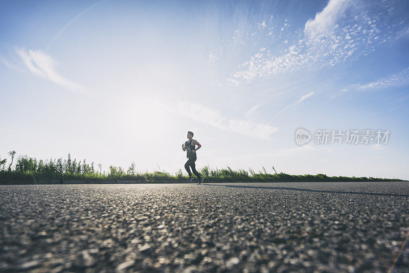 年轻的男运动员在柏油路上迎着天空奔跑