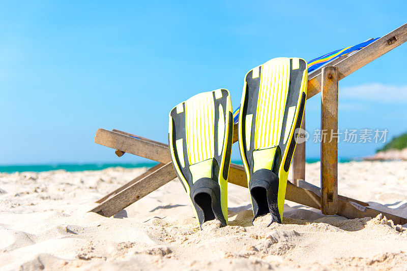夏天的一天。黄色的鱼鳍躺在沙滩上，在阳光明媚的夏日，蓝天为背景。旅游与夏日概念