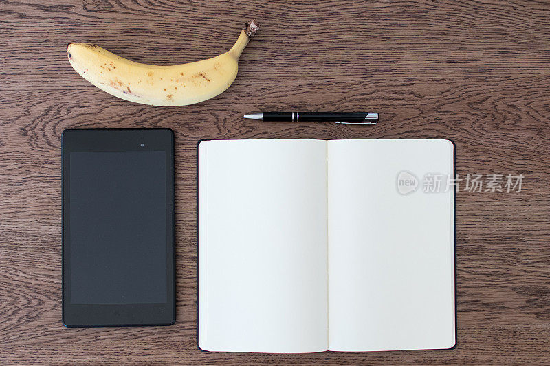 木桌上放着写字板、笔记本、笔和一根香蕉。假新闻的概念